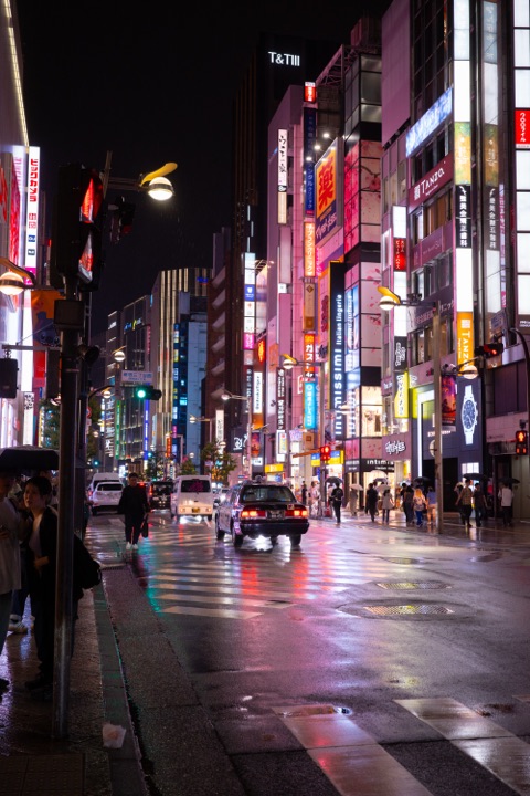 A wet street at night lined with glowing neon signs reflecting off the road